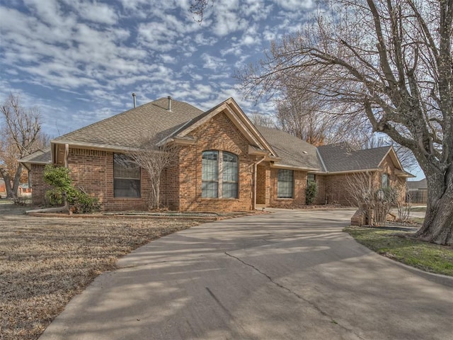 view of front of property featuring brick siding, roof with shingles, and concrete driveway