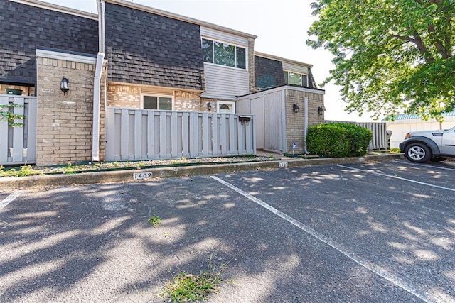 exterior space with fence, roof with shingles, mansard roof, uncovered parking, and brick siding