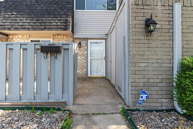 entrance to property featuring brick siding, mansard roof, and a shingled roof