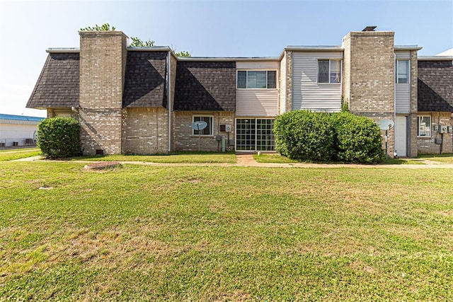 rear view of property with roof with shingles, mansard roof, a chimney, a lawn, and brick siding