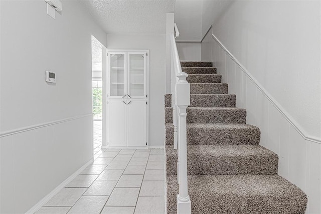 stairway featuring tile patterned flooring, wainscoting, and a textured ceiling