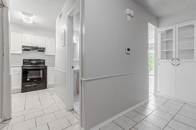 kitchen featuring under cabinet range hood, a wainscoted wall, black electric range oven, and a textured ceiling