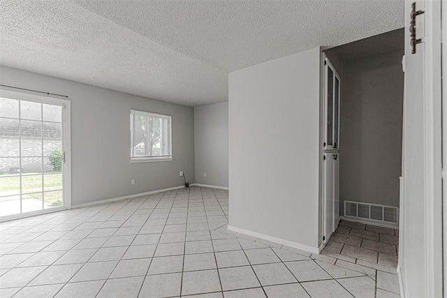 empty room with light tile patterned floors, baseboards, visible vents, and a textured ceiling