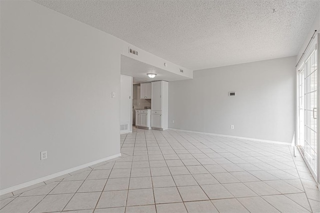 empty room with light tile patterned flooring, visible vents, a textured ceiling, and baseboards