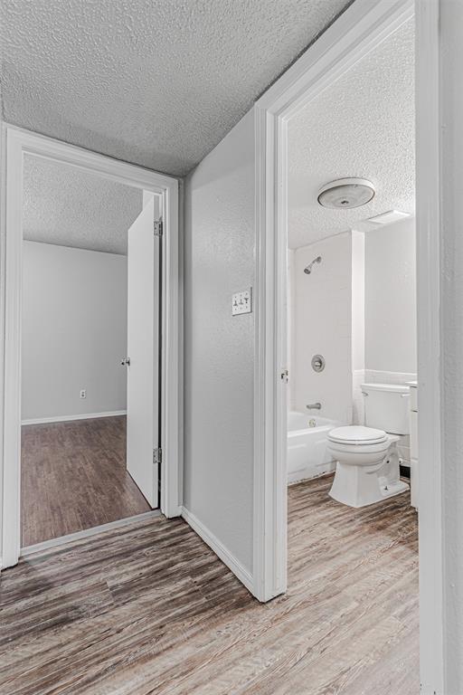 hallway with a textured ceiling, baseboards, and wood finished floors