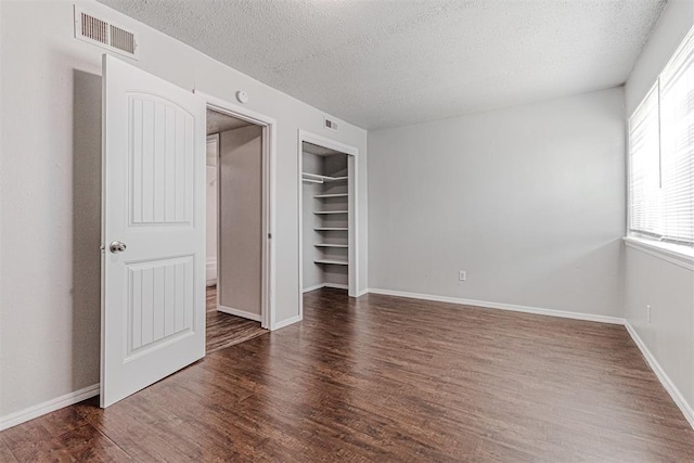 unfurnished bedroom featuring visible vents, baseboards, wood finished floors, a closet, and a textured ceiling