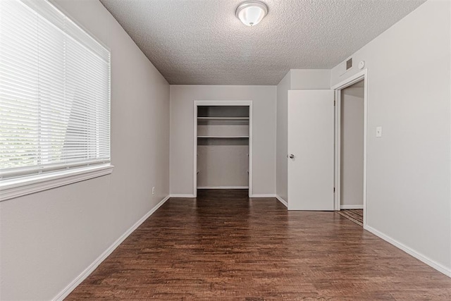 unfurnished bedroom featuring a closet, a textured ceiling, baseboards, and wood finished floors