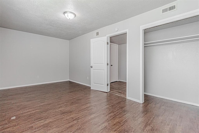 unfurnished bedroom with a closet, visible vents, a textured ceiling, and wood finished floors