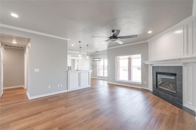 unfurnished living room with visible vents, light wood-style flooring, a ceiling fan, ornamental molding, and a tile fireplace