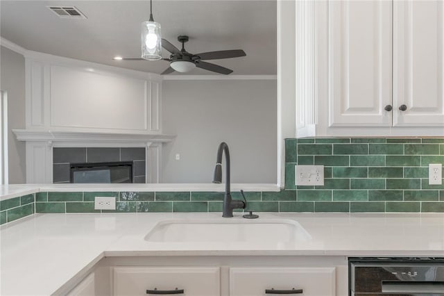 kitchen featuring visible vents, a sink, backsplash, white cabinetry, and a tile fireplace