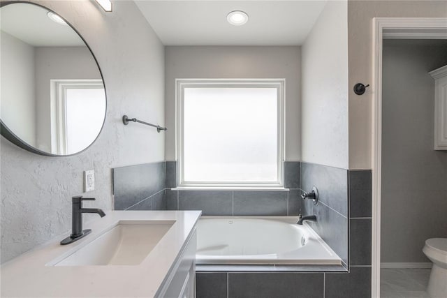 bathroom featuring toilet, vanity, a garden tub, and a textured wall