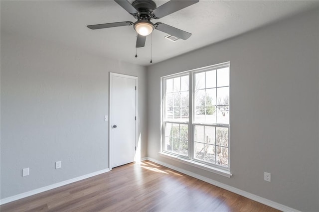 empty room with a ceiling fan, wood finished floors, visible vents, and baseboards