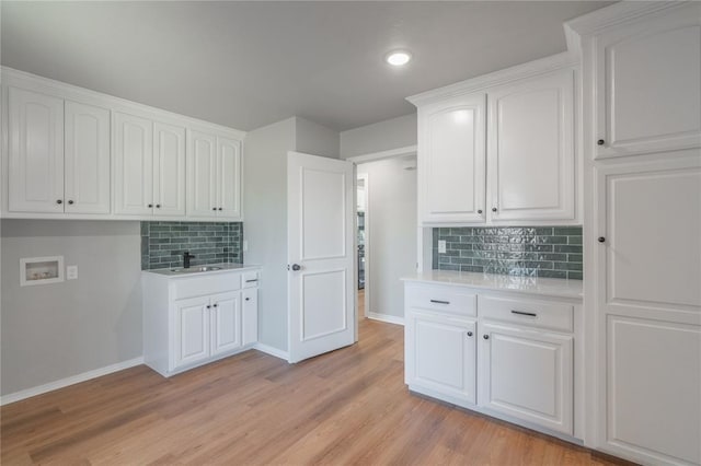 kitchen with light wood-style flooring, a sink, white cabinets, light countertops, and baseboards