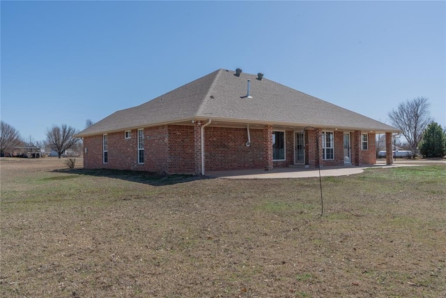 back of house featuring a patio, a lawn, brick siding, and roof with shingles