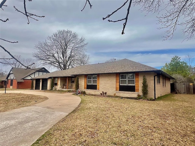 view of front facade featuring brick siding, a front lawn, fence, roof with shingles, and driveway