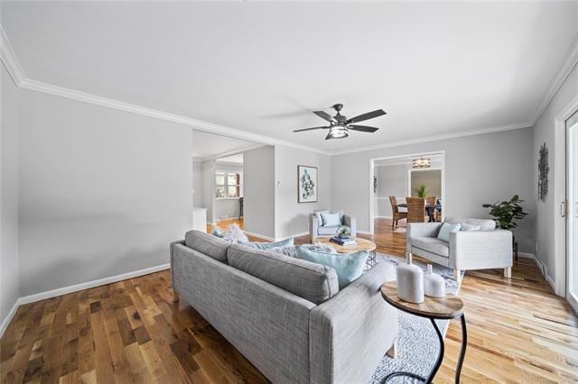 living room with a ceiling fan, crown molding, baseboards, and wood finished floors