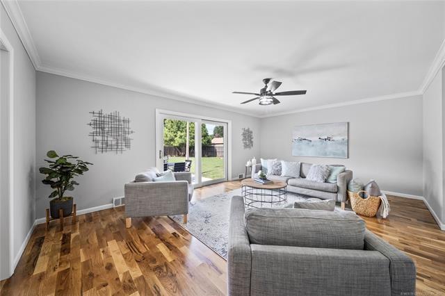 living area with baseboards, a ceiling fan, wood finished floors, and crown molding