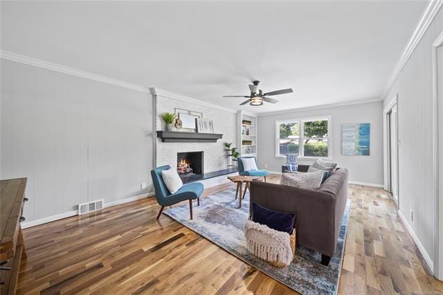 living room with visible vents, ornamental molding, a fireplace, wood finished floors, and a ceiling fan