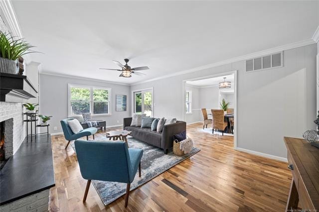 living area featuring wood finished floors, visible vents, a warm lit fireplace, and baseboards