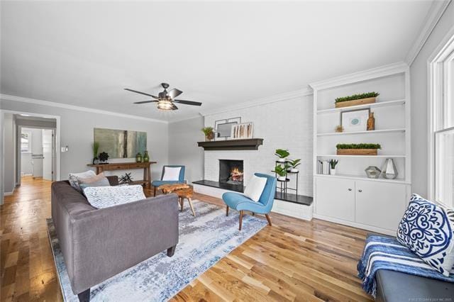 living area featuring ceiling fan, crown molding, light wood finished floors, and a large fireplace