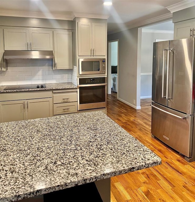 kitchen featuring ornamental molding, under cabinet range hood, appliances with stainless steel finishes, decorative backsplash, and light stone countertops