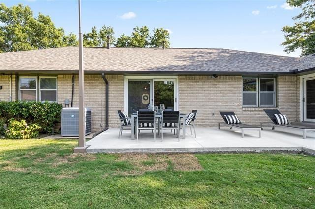 rear view of house featuring brick siding, a lawn, a patio, and central AC