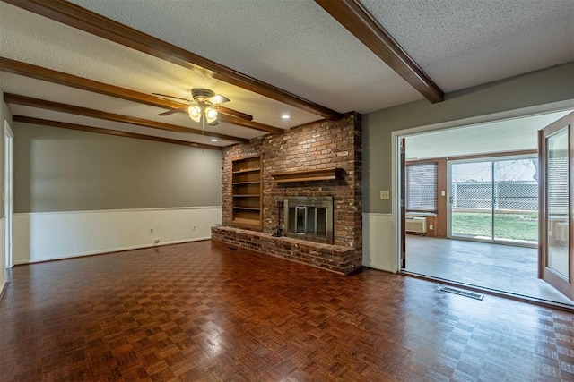 unfurnished living room featuring beamed ceiling, built in shelves, a textured ceiling, a brick fireplace, and ceiling fan