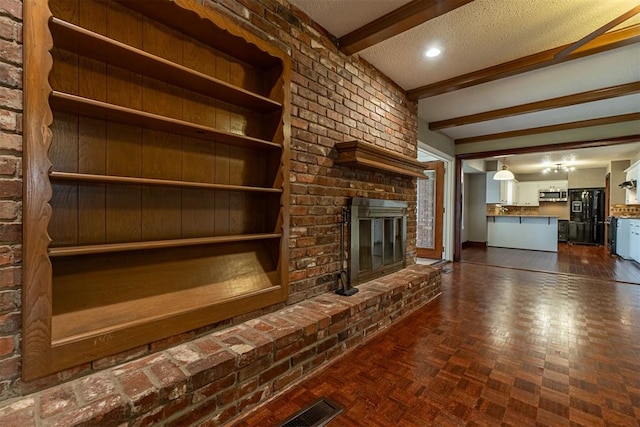 unfurnished living room with visible vents, brick wall, beam ceiling, a fireplace, and a textured ceiling