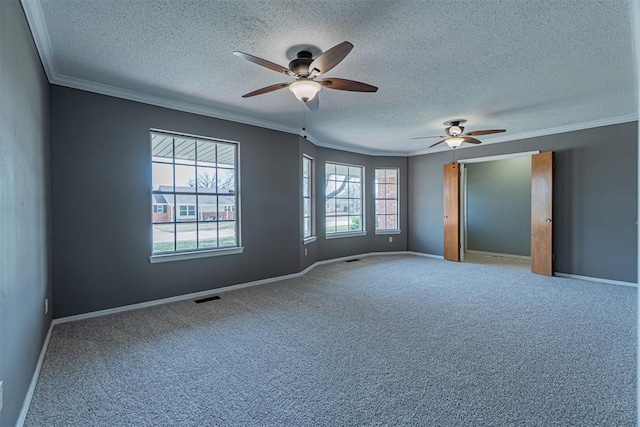 carpeted spare room with visible vents, baseboards, a ceiling fan, and ornamental molding