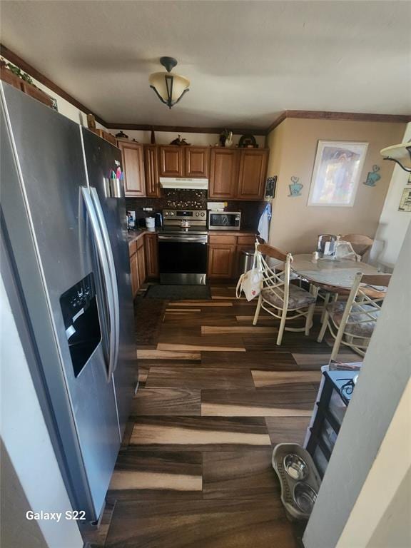 kitchen featuring under cabinet range hood, appliances with stainless steel finishes, ornamental molding, and brown cabinetry