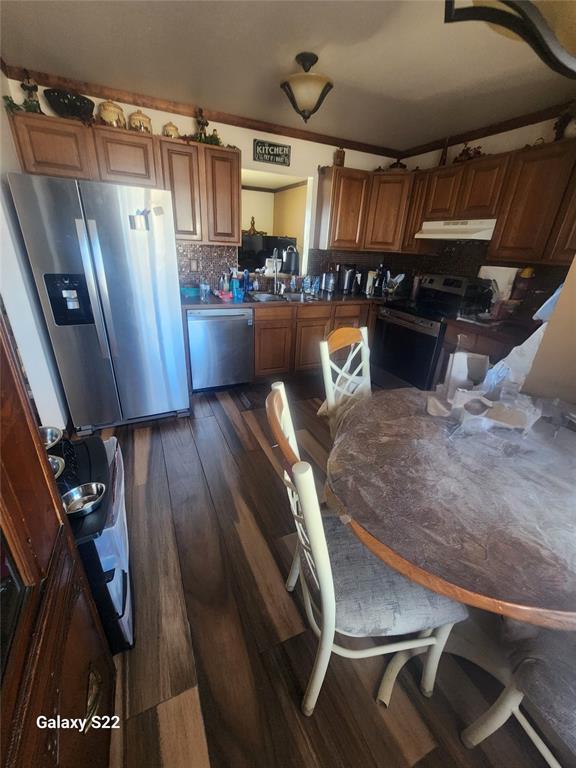 kitchen featuring brown cabinetry, dark wood-style flooring, under cabinet range hood, and stainless steel appliances