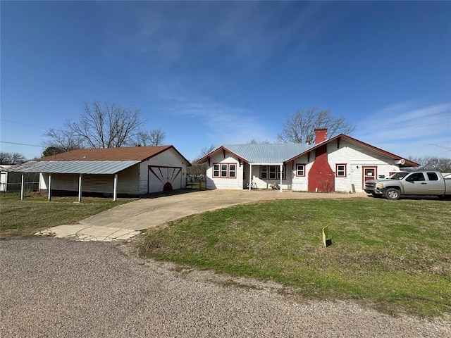 ranch-style house with a front lawn, metal roof, a chimney, concrete driveway, and an outbuilding
