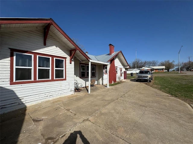 view of side of home featuring a lawn, a chimney, and metal roof