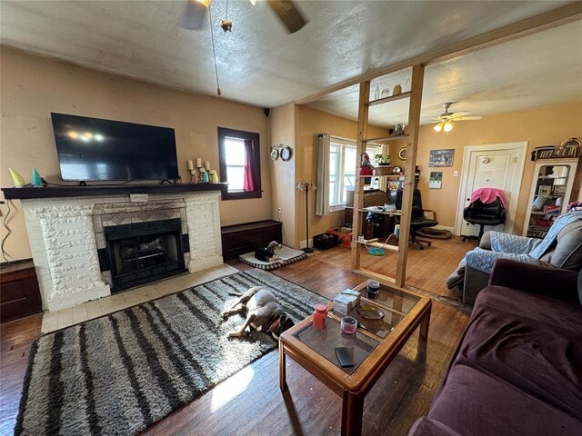 living area with a stone fireplace, a ceiling fan, a textured ceiling, and wood finished floors