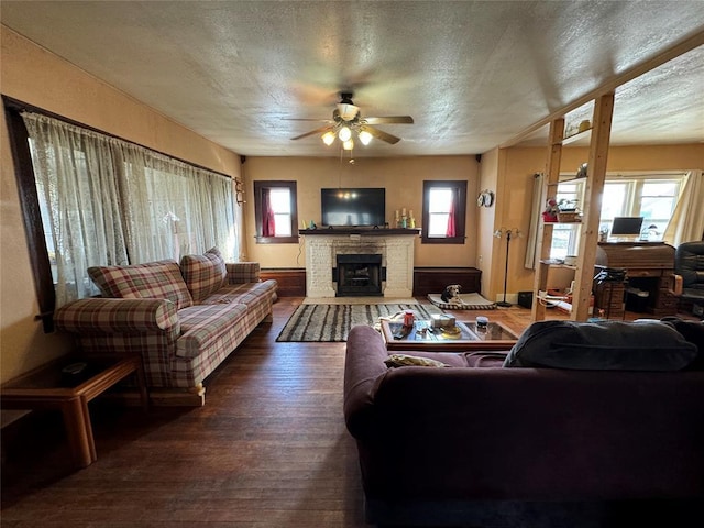 living area featuring a brick fireplace, a healthy amount of sunlight, ceiling fan, a textured ceiling, and hardwood / wood-style flooring