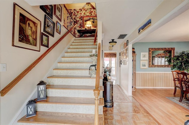 staircase featuring visible vents, wainscoting, and parquet floors