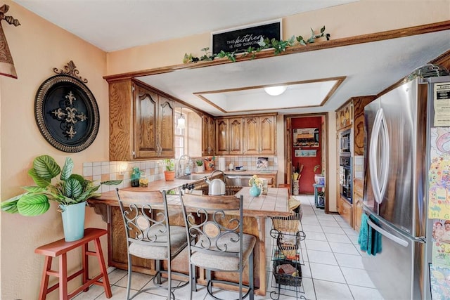 kitchen with a kitchen bar, freestanding refrigerator, a peninsula, light tile patterned floors, and decorative backsplash