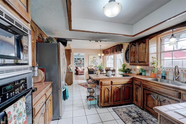 kitchen featuring tile countertops, a peninsula, a sink, black appliances, and decorative light fixtures