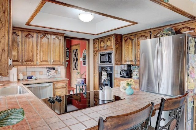 kitchen with a sink, tasteful backsplash, black appliances, and tile counters