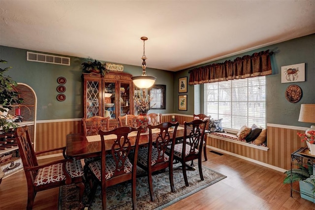 dining space featuring wood finished floors, visible vents, and wainscoting