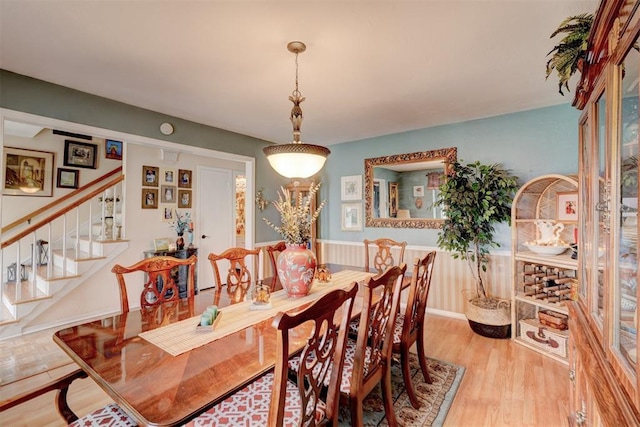 dining room featuring stairway, light wood-style floors, and wainscoting