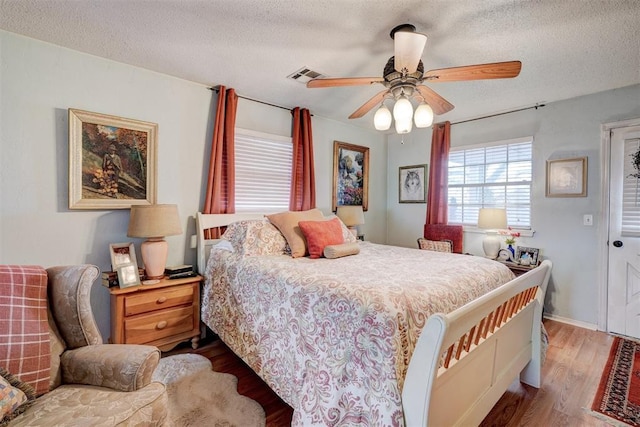 bedroom with ceiling fan, visible vents, a textured ceiling, and wood finished floors