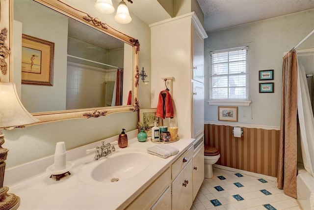 bathroom with a wainscoted wall, toilet, a shower with shower curtain, a textured ceiling, and vanity