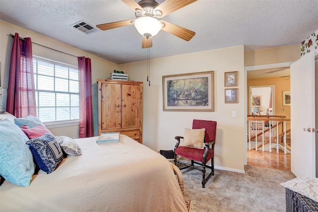 bedroom with baseboards, visible vents, ceiling fan, a textured ceiling, and light carpet