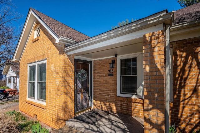 entrance to property with brick siding and roof with shingles