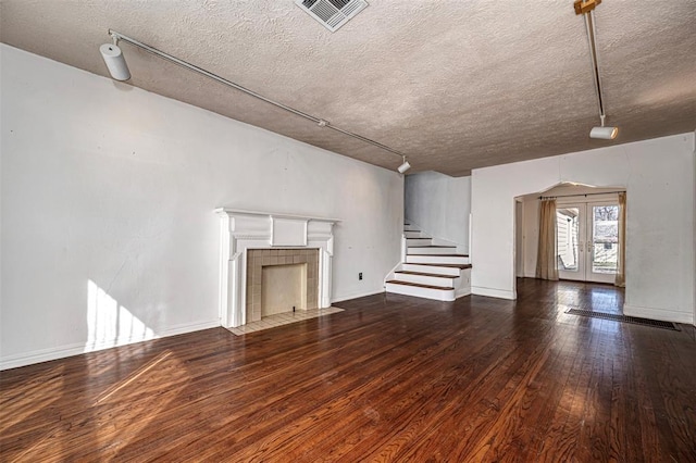 unfurnished living room with visible vents, hardwood / wood-style floors, french doors, a fireplace, and stairs