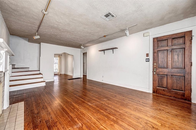 unfurnished living room featuring visible vents, track lighting, stairway, hardwood / wood-style flooring, and a textured ceiling