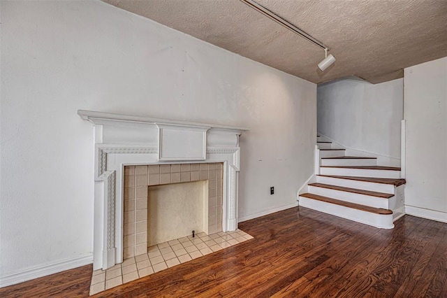 unfurnished living room featuring a fireplace, stairway, wood finished floors, and a textured ceiling