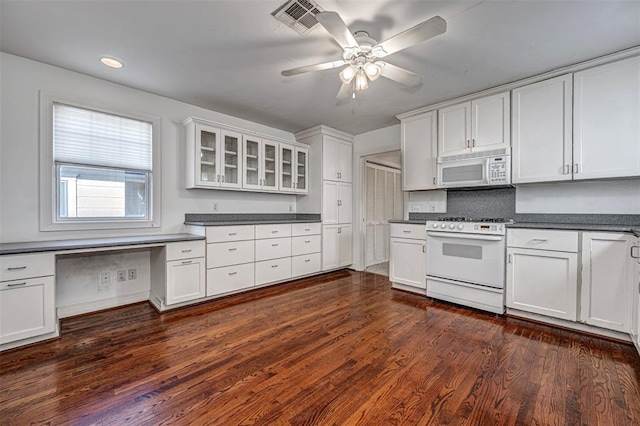 kitchen featuring dark countertops, visible vents, dark wood finished floors, built in desk, and white appliances