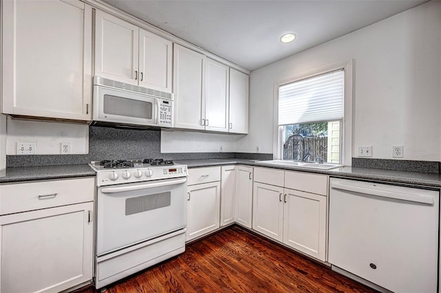 kitchen featuring dark countertops, white cabinets, white appliances, and a sink